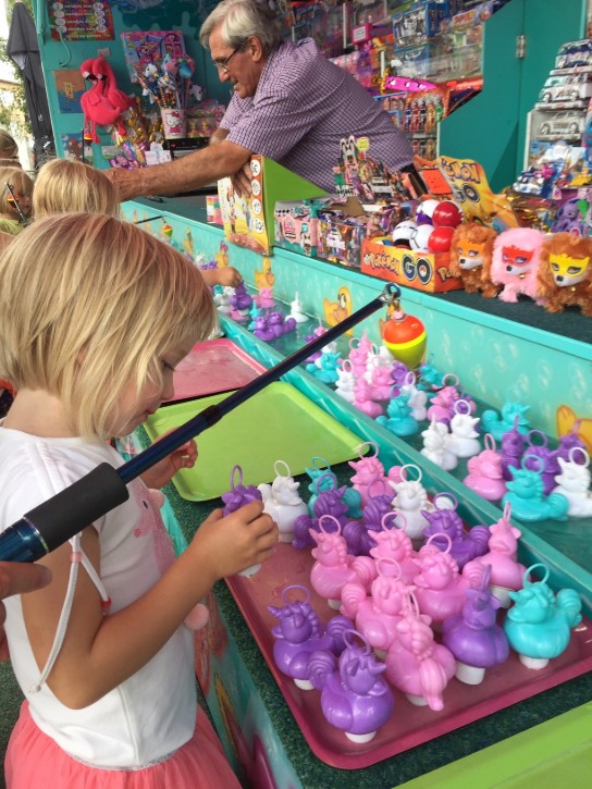 Kind speelt met hengel bij een kraam vol kleurrijke eenhoornfiguren op een kermis. (vergroot foto)